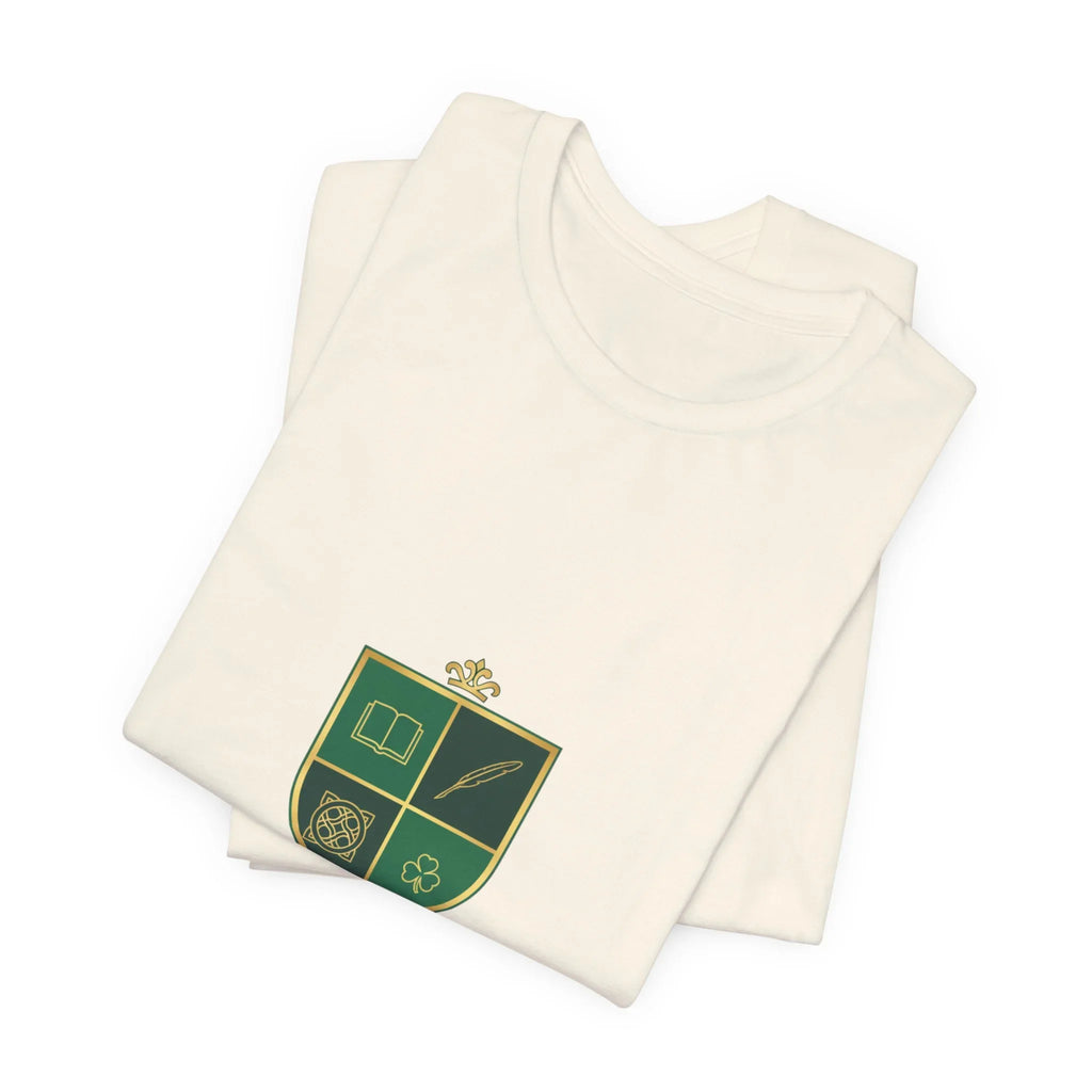 Folded white t-shirt with green and gold crest featuring book, feather, knot, and clover symbols