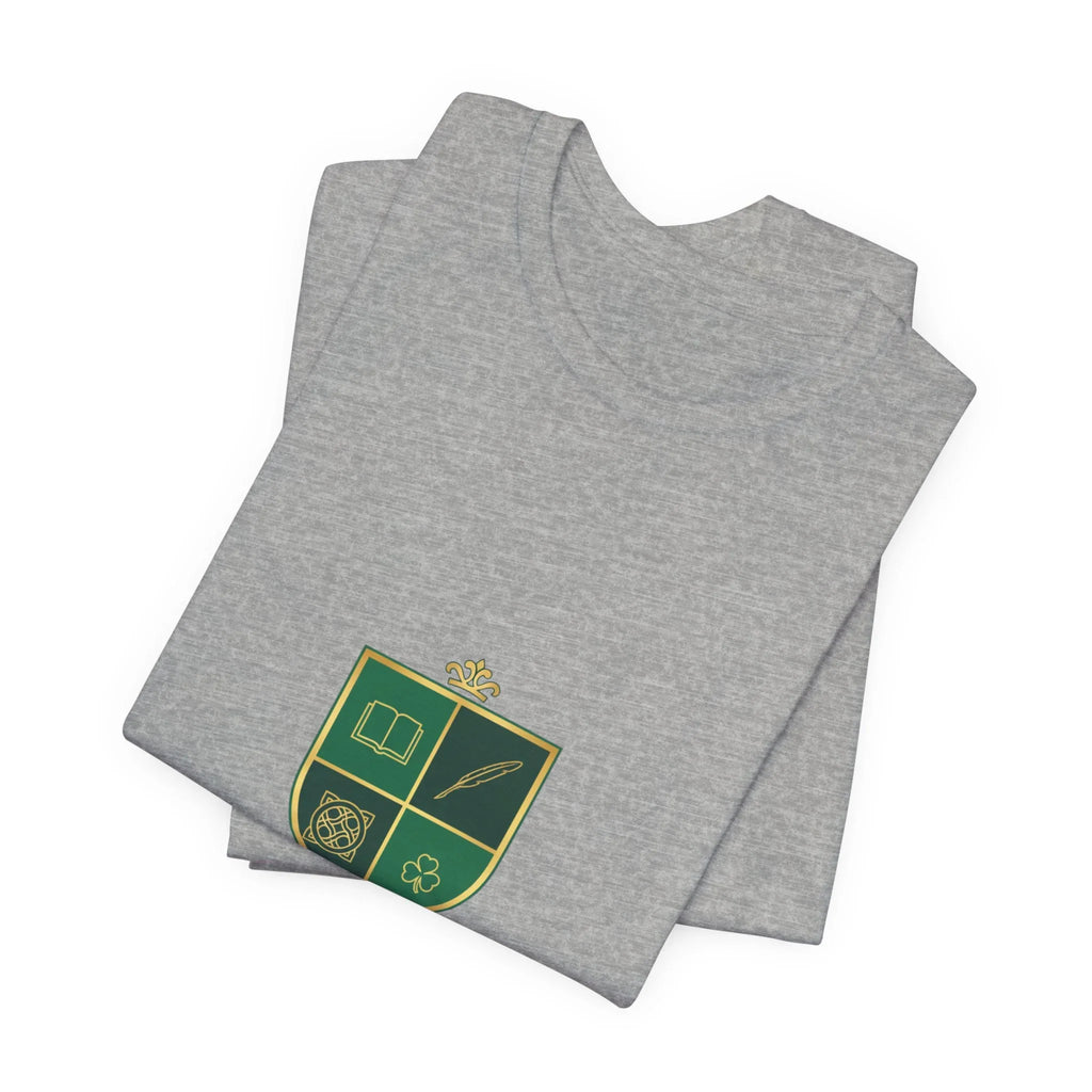 Folded grey t-shirt with green and gold crest featuring book, feather, knot, and clover icons
