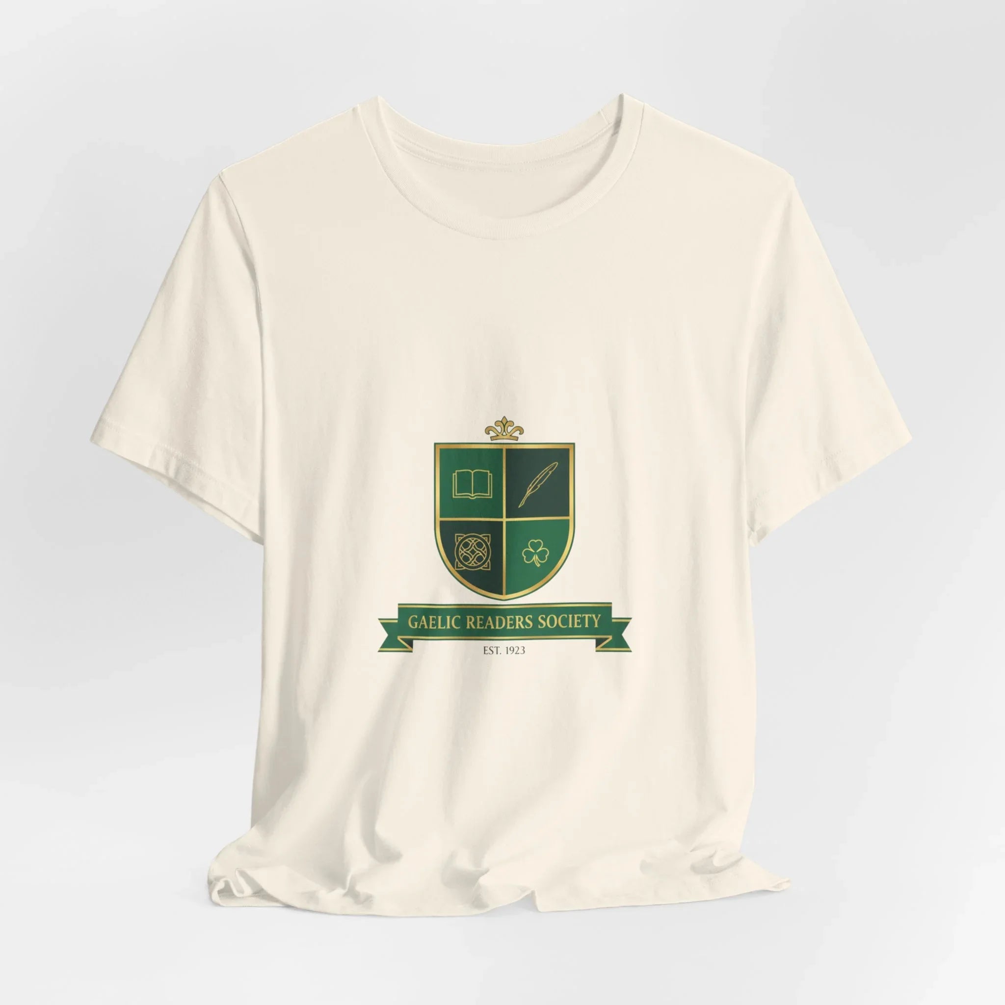 Cream t-shirt with green Gaelic Readers Society crest and ribbon, featuring book, quill, knot, and shamrock icons.